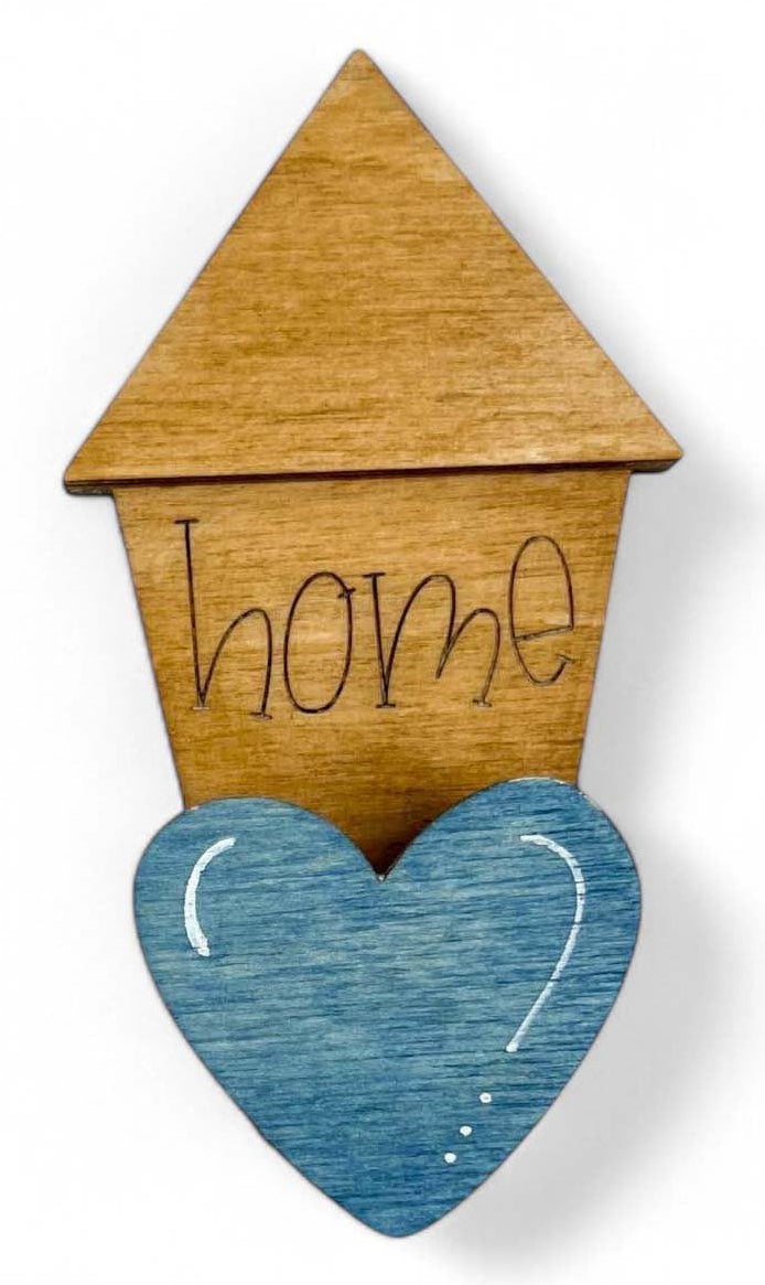 A wooden mug hugger in the shape of a house with a heart on the front